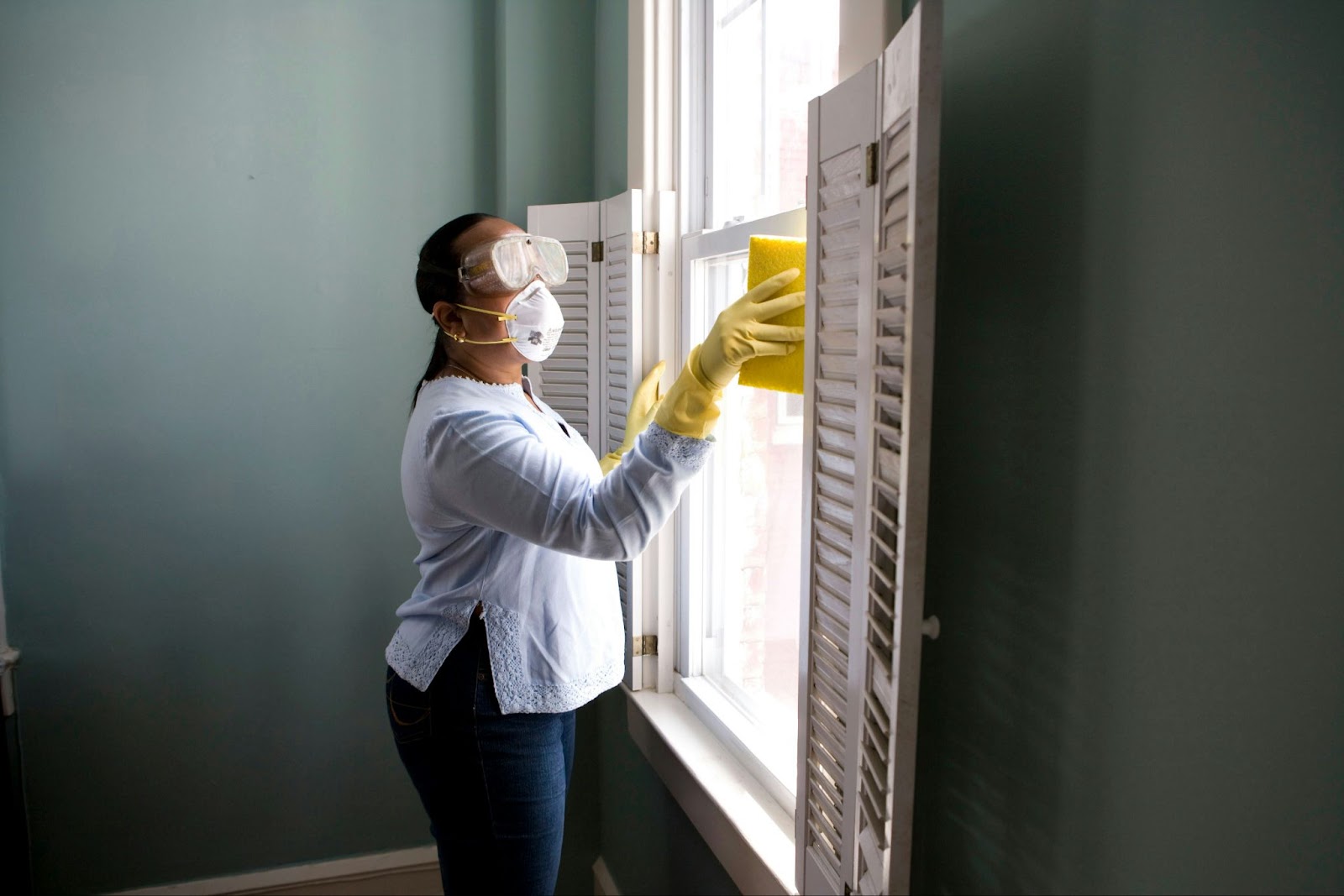 A woman wearing protective equipment while cleaning a window, ensuring safety during chemical cleaning tasks