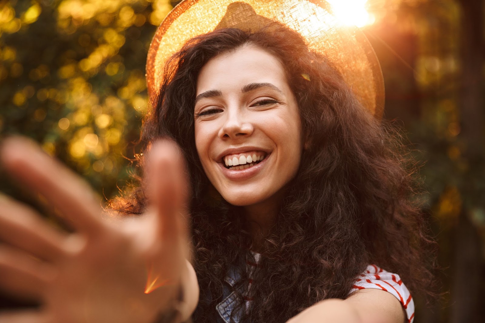 Woman in a hat smiling with the sun in the background. 