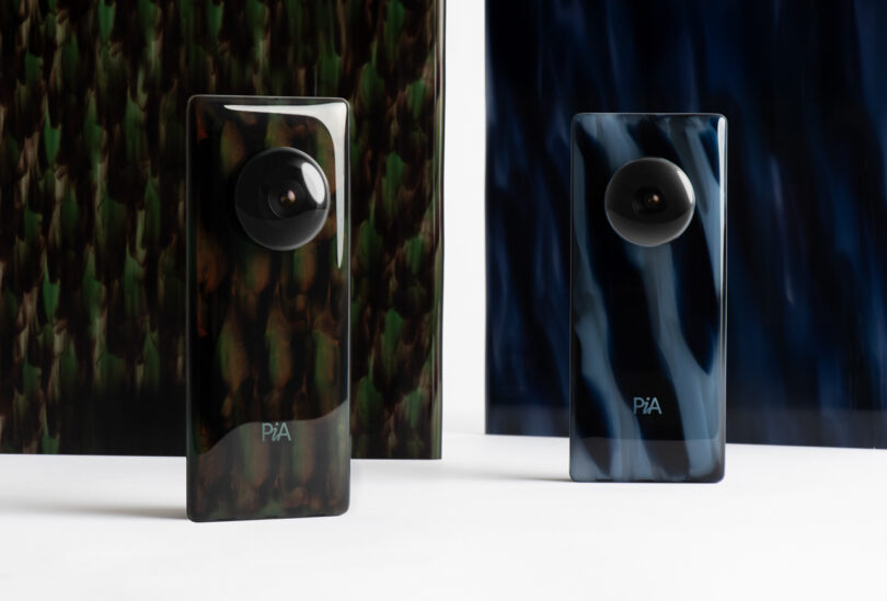 Two sleek, modern smartphones with circular camera lenses standing upright on a white surface. One has a dark brown pattern, the other a dark blue pattern. Background features similar patterns.