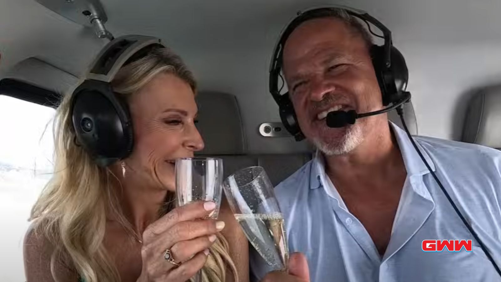 Joan and Keith in a helicopter, toasting champagne with headsets on.