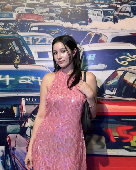 This contain Lea Navvab Huening
 in a pink dress standing next to a wall with many cars on it