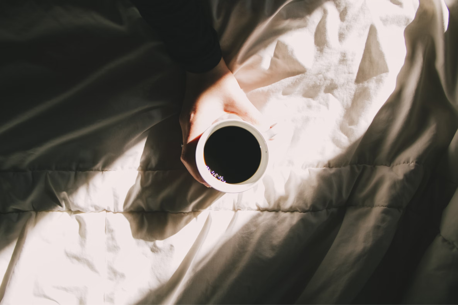 Coffee in white mug on white bedsheets