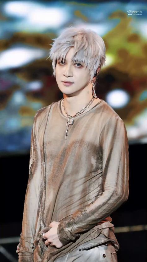 This contains an image of Joker Xue with white hair standing in front of a large screen and wearing silver pants