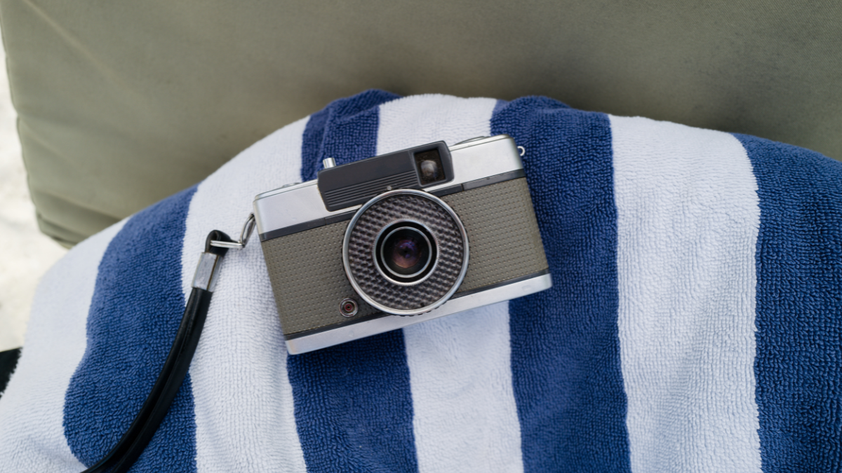 A vintage camera resting on a striped blue and white towel, evoking a nostalgic and relaxed summer vibe.