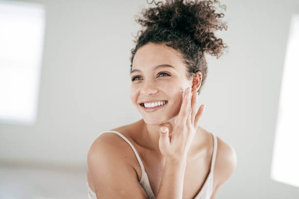 A happy woman with a bright smile and flawless skin, lightly touching her face, reflecting the benefits of a vitamin-rich skincare routine.