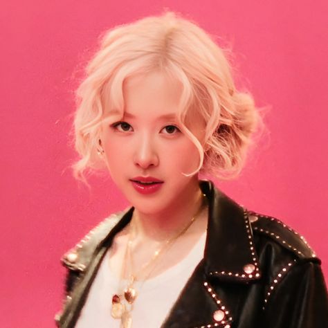 This  contain Rosé with blonde hair wearing a black leather jacket and pearl necklace, standing in front of a pink background