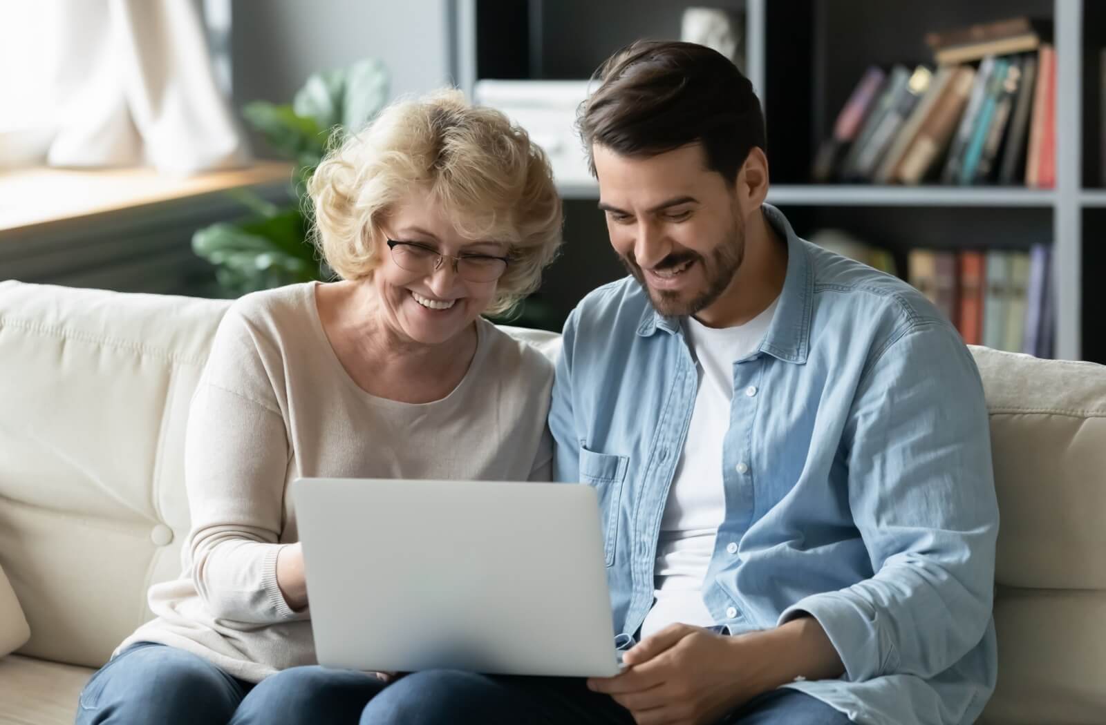 A senior smiles while exploring memory care communities on a laptop with their child.