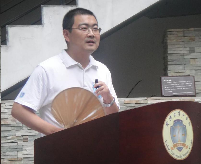 Profile picture of an Asian man standing behind a podium. He has short, dark hair and he’s wearing rectangular glasses. In one hand he holds a fan, in the other a microphone. He is wearing a white short-sleeved polo.