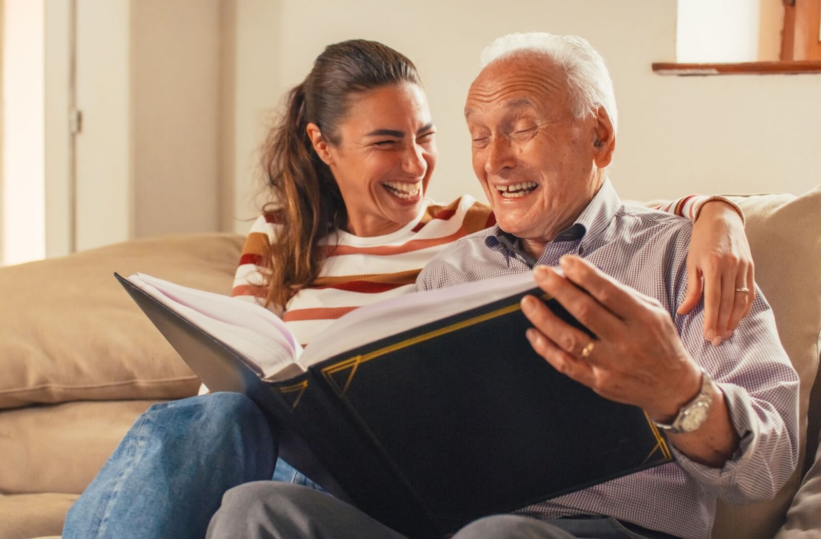 A senior and their child laugh together as they look through a book of memories.