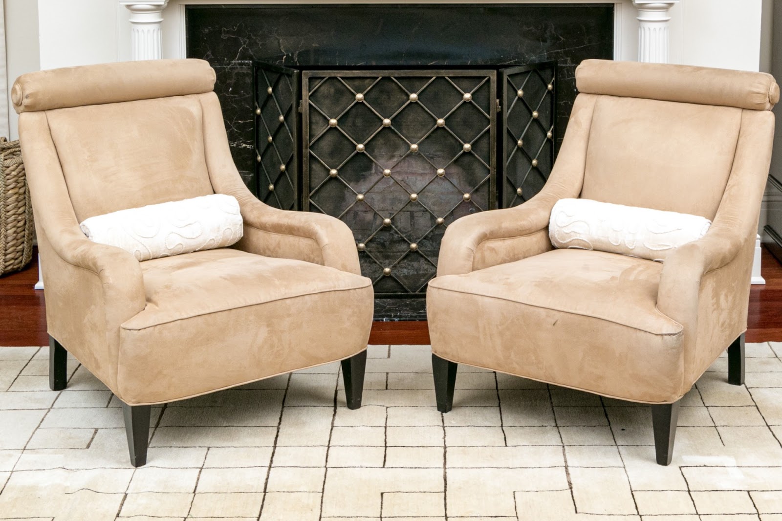 a Pair of creamy beige suede Upholstered Armchairs with white velvet bolster pillows in front of a fireplace.