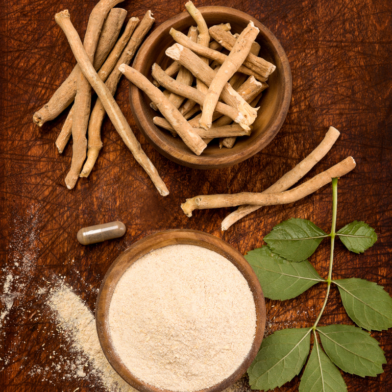A bowl of ashwagandha powder and leaves sits on a rustic wooden table.