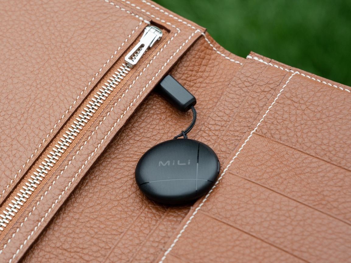 A black round device attached to a brown leather wallet

Description automatically generated