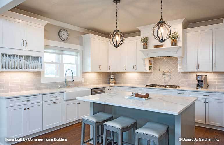Kitchen with white cabinetry, gray subway tile backsplash, and a breakfast island well-lit by a couple of spherical pendants.
