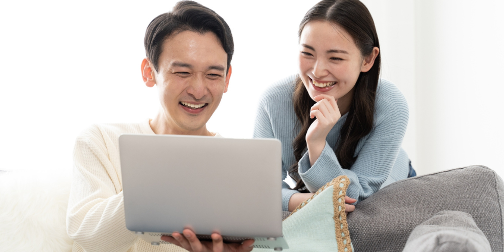 リビングでノートＰＣ画面を見ながら笑顔を交わす若い夫婦