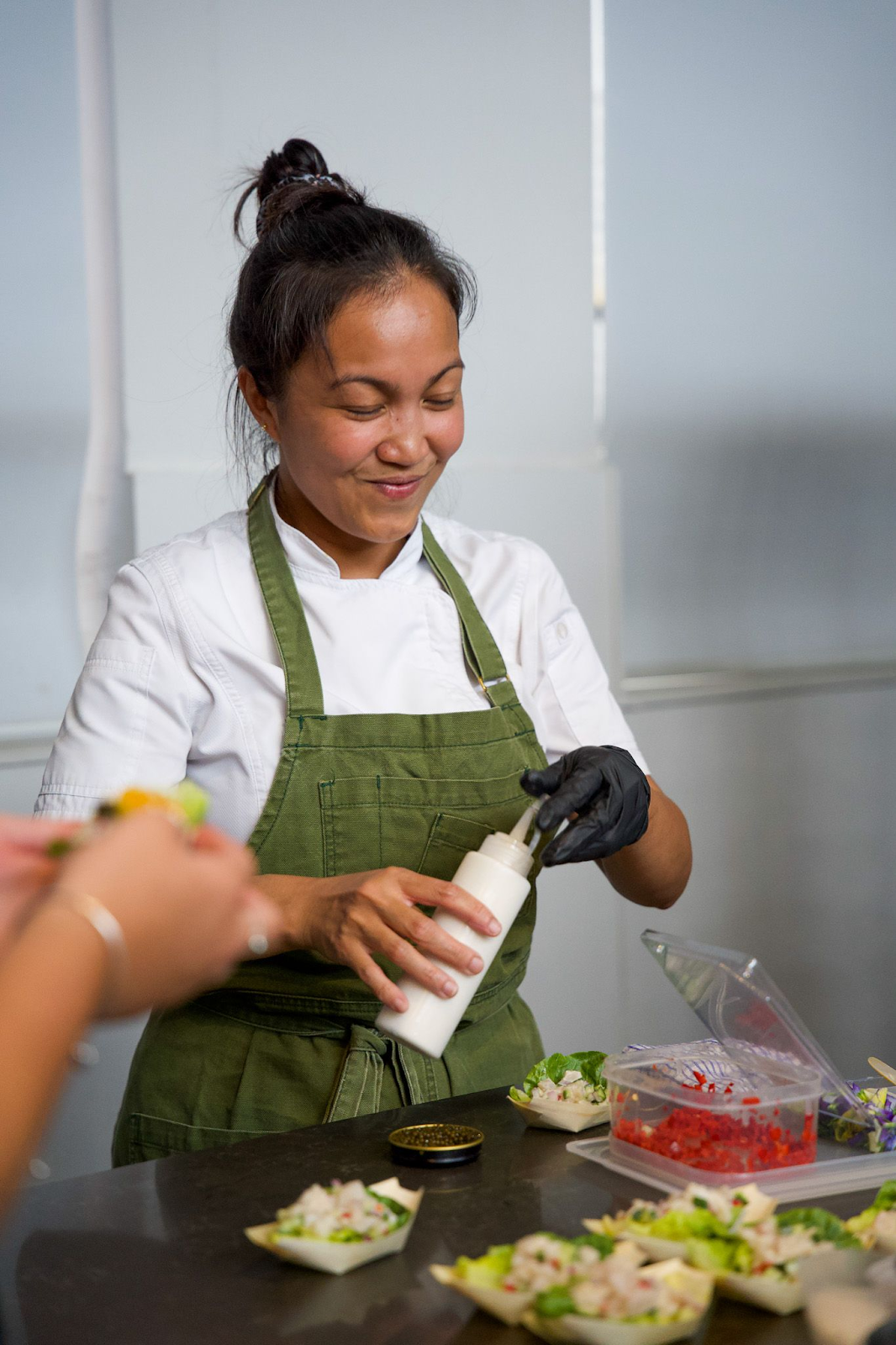 A person wearing a green apron and black glovesDescription automatically generated