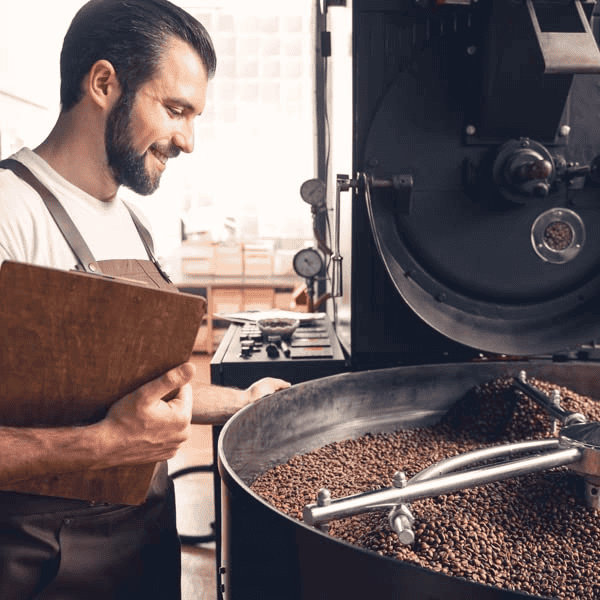 "An image of a man standing amidst piles of freshly harvested coffee beans, gazing thoughtfully at the rows of beans that will be processed into coffee. The beans are spread out evenly on large drying trays, with the natural sunlight illuminating the scene, reflecting the beginnings of a traditional coffee-making process."