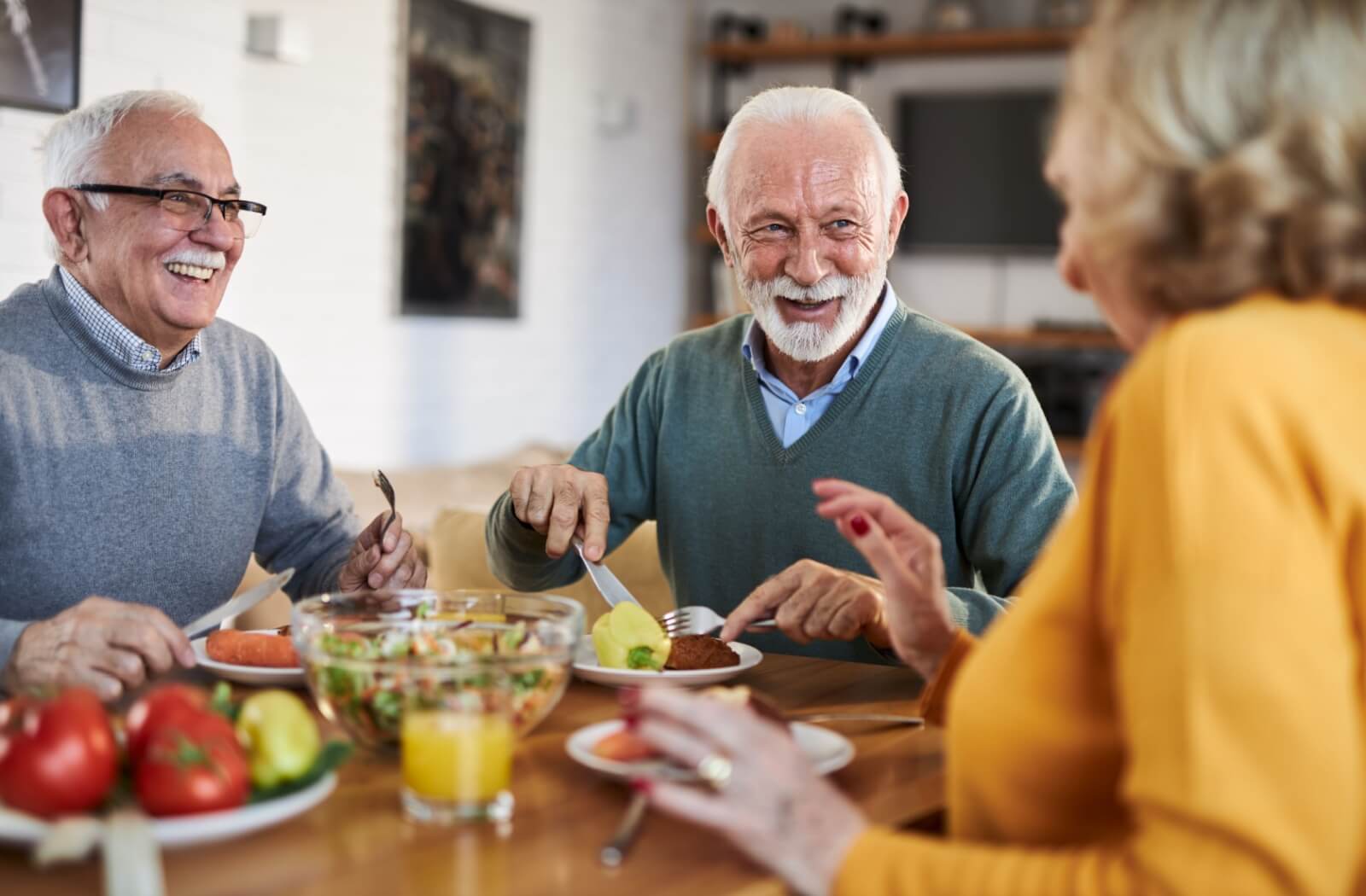 A group of seniors laugh together over a healthy meal in a senior living community