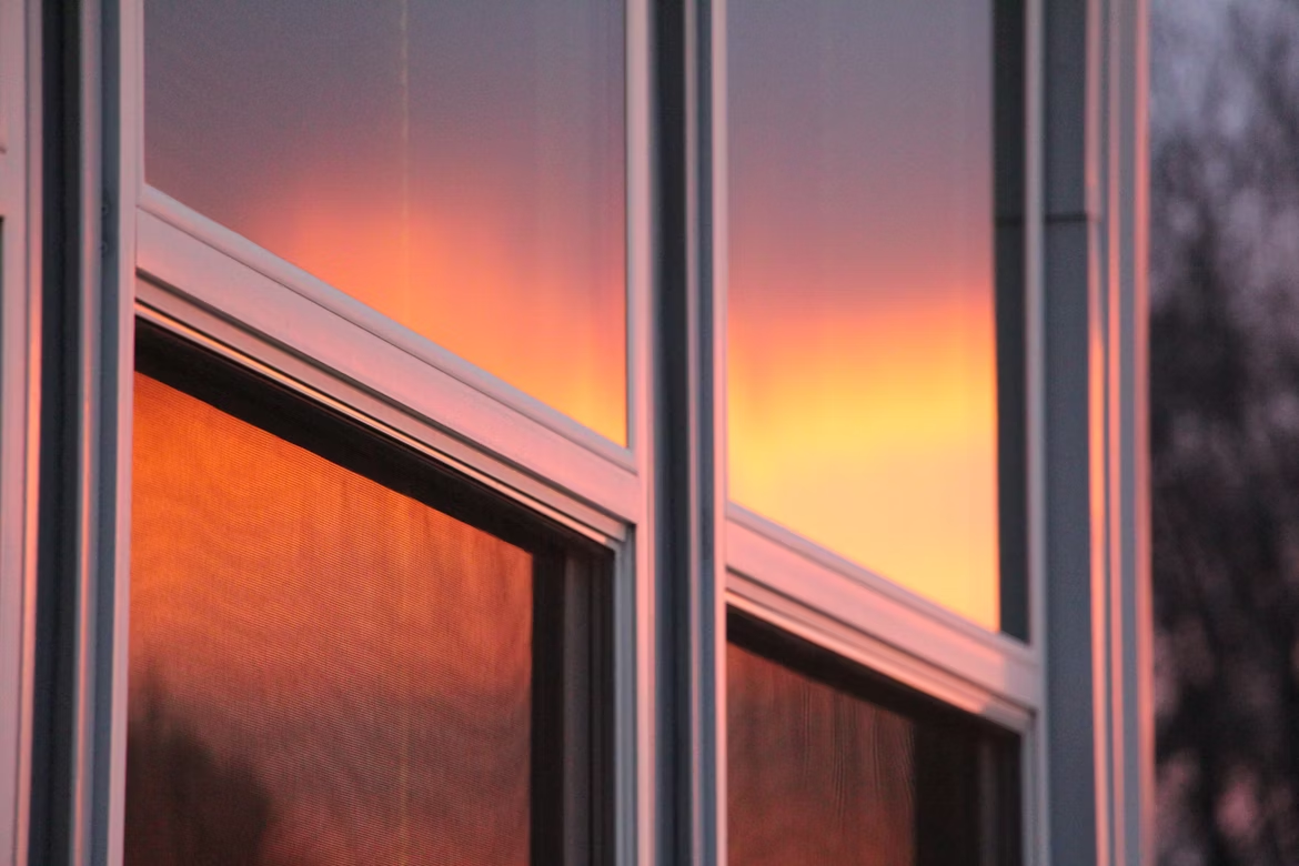 Close-up of modern window panes reflecting a vivid orange and pink sunset, creating a warm glow on the building’s exterior.