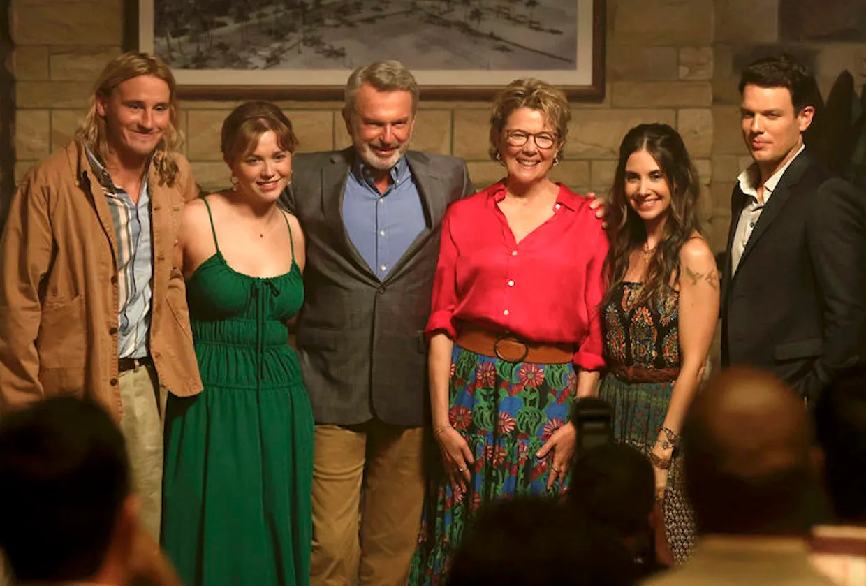 Grupo de seis personas posando para una foto en un ambiente interior. De izquierda a derecha: un hombre con chaqueta beige, una mujer con vestido verde, un hombre con saco gris, una mujer con blusa roja y falda colorida, una mujer con vestido estampado y un hombre con saco negro.