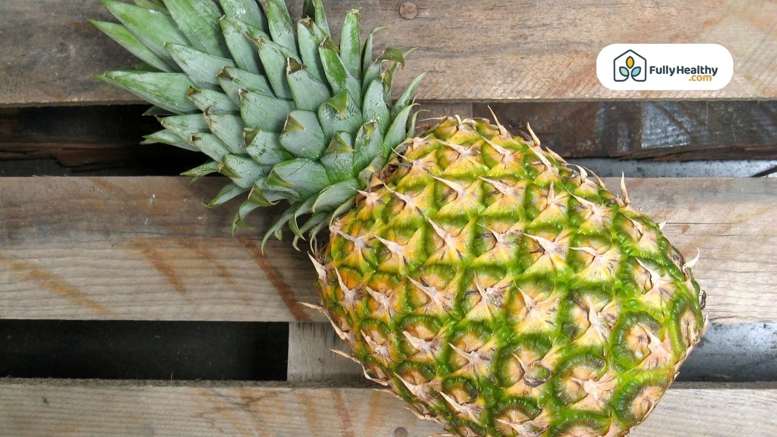 Whole fresh pineapple on wooden pallet with FullyHealthy logo