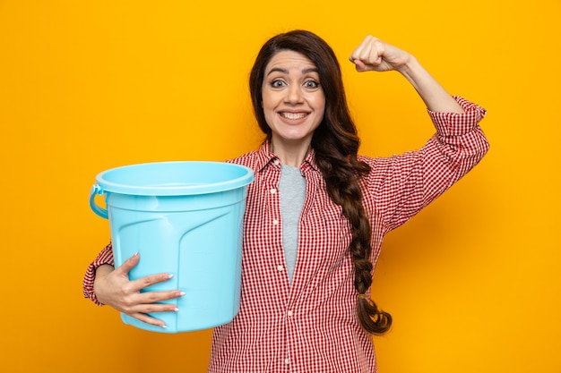 Smiling pretty caucasian cleaner woman holding bucket and tensing biceps 