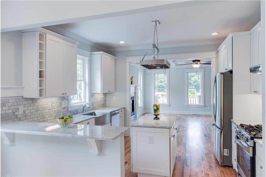 The kitchen is equipped with stainless steel appliances, white cabinetry, a center island, and a marble top snack bar.