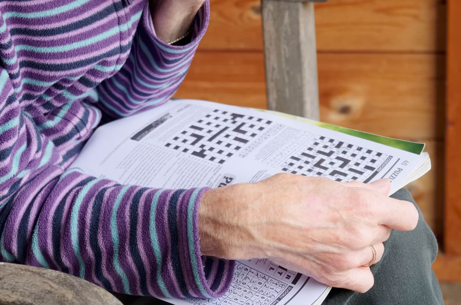 A close-up image of an older adult holding an open book with crossword puzzles.
