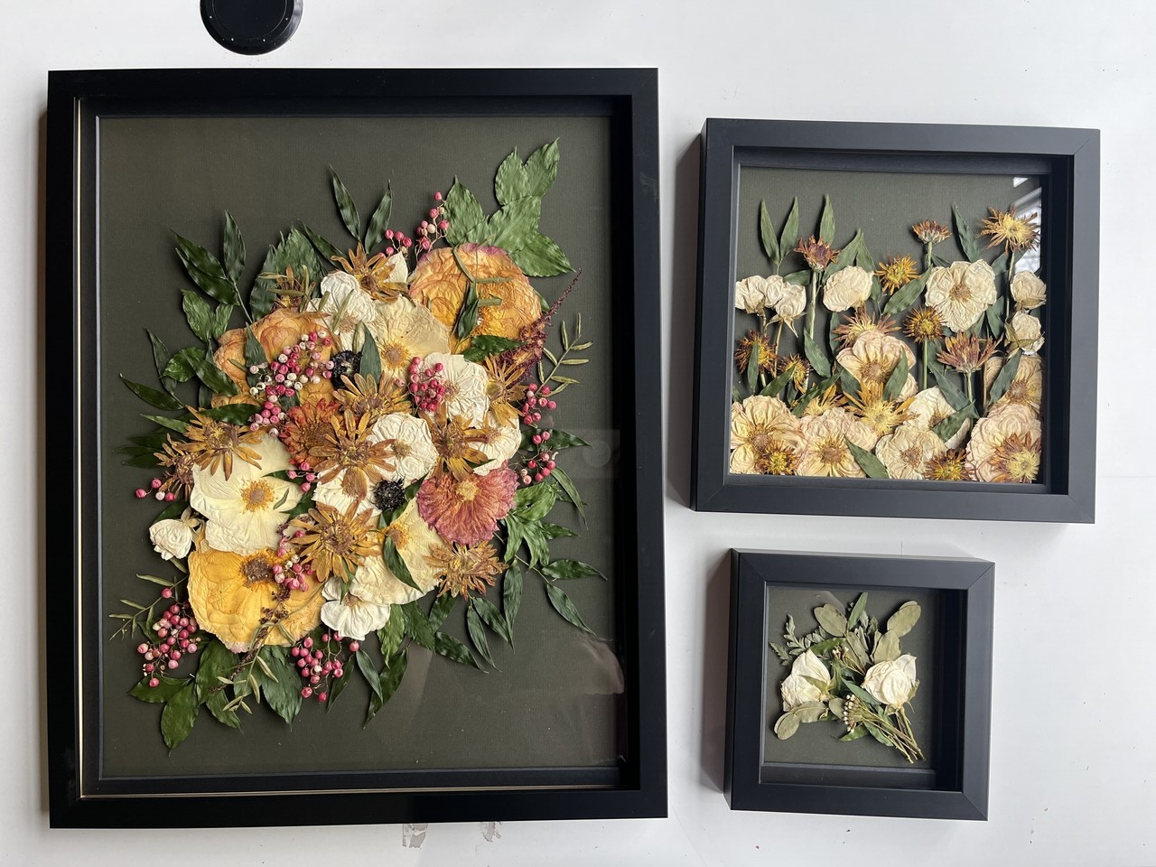 large, medium, and small black frames with pressed flowers encased with a black background