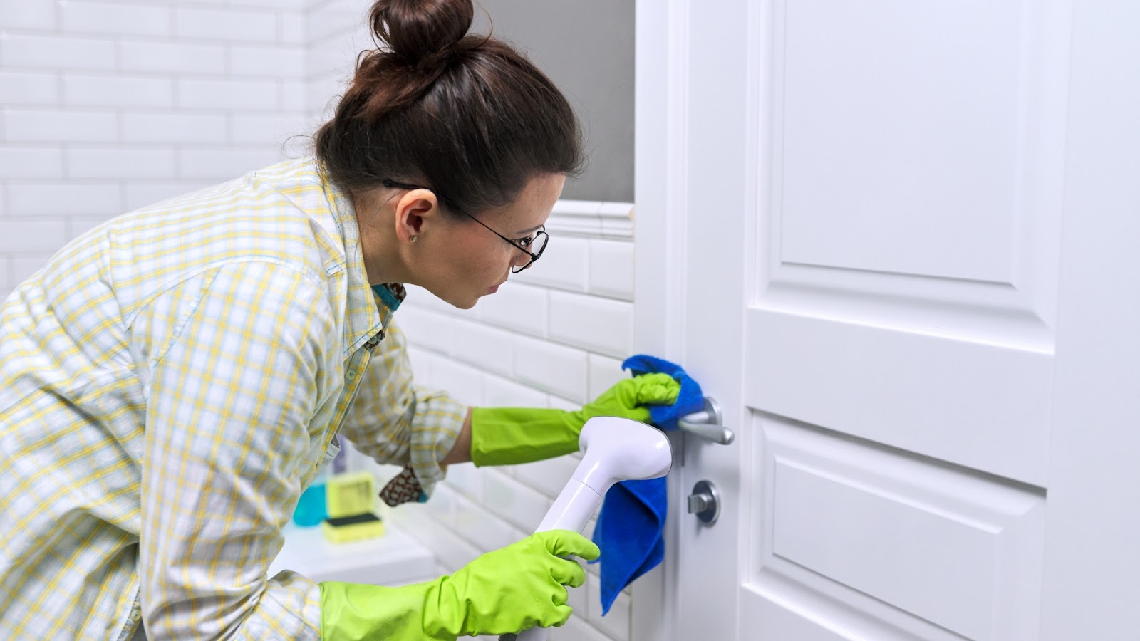 A woman cleaning a door handle with gloves and steam cleaner.