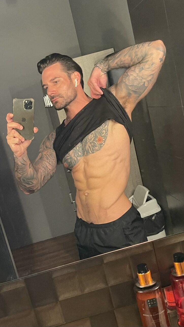 Papi Kocic taking an iphone mirror selfie  lifting his black tank top to reveal his abs and tattooed pecs for onlyfans gay xxx porn content