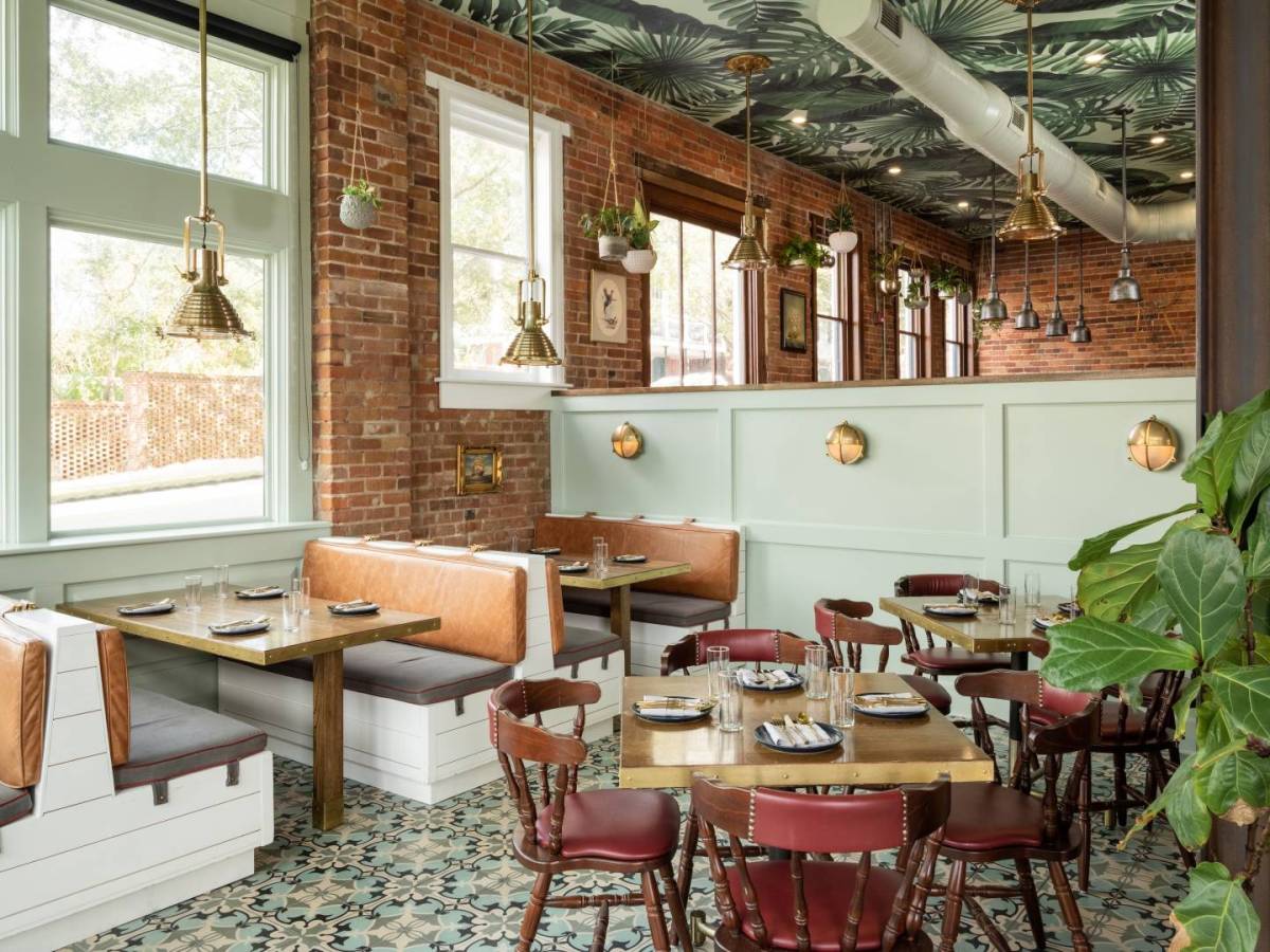 A photo of Wilmington restaurant Drm Yard, with brick walls, rustic seating, and a palm frond-patterned ceiling