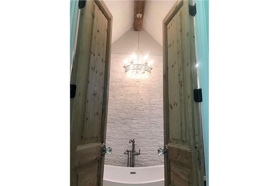 Primary bathroom with a double door and a cathedral ceiling lined with a wood beam.