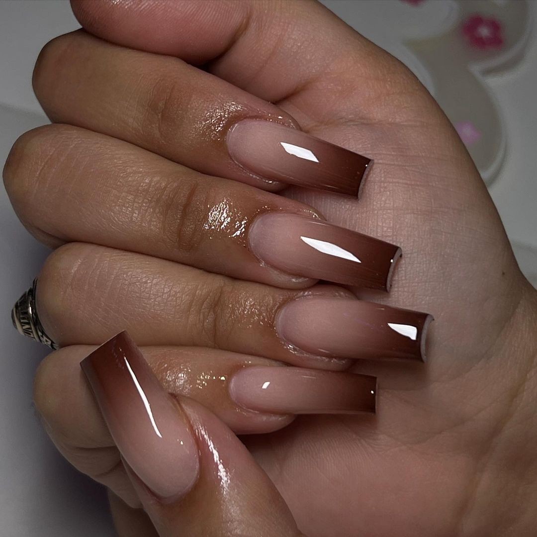 Close-up of hands with glossy, long, brown nails featuring a white V-shaped design on each.

