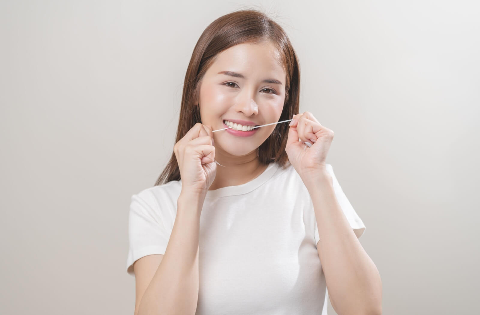 a person grinning while flossing in between teeth to practice good dental hygiene and keep a healthy smile