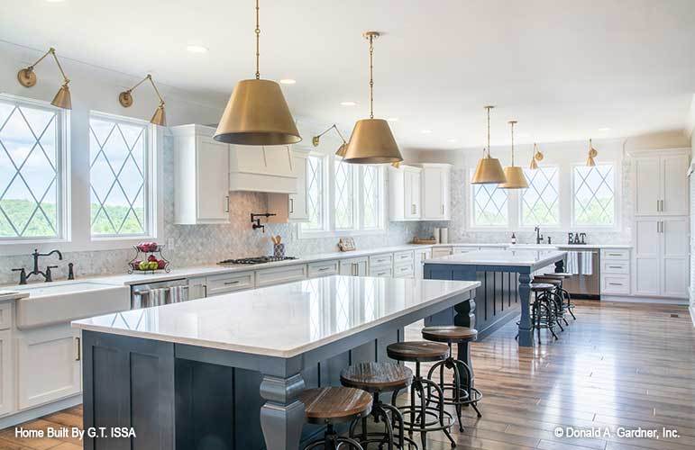 Kitchen with white cabinetry, two islands, and matching brass sconces and dome pendants.
