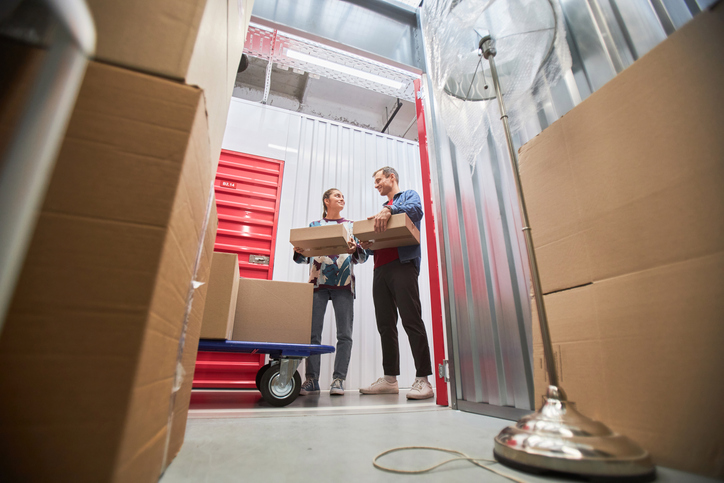 A man and woman moving boxes into a storage unit. 