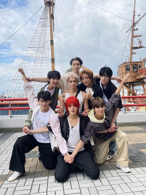 This may contain a group of NCT 127 posing for a photo in front of a ship