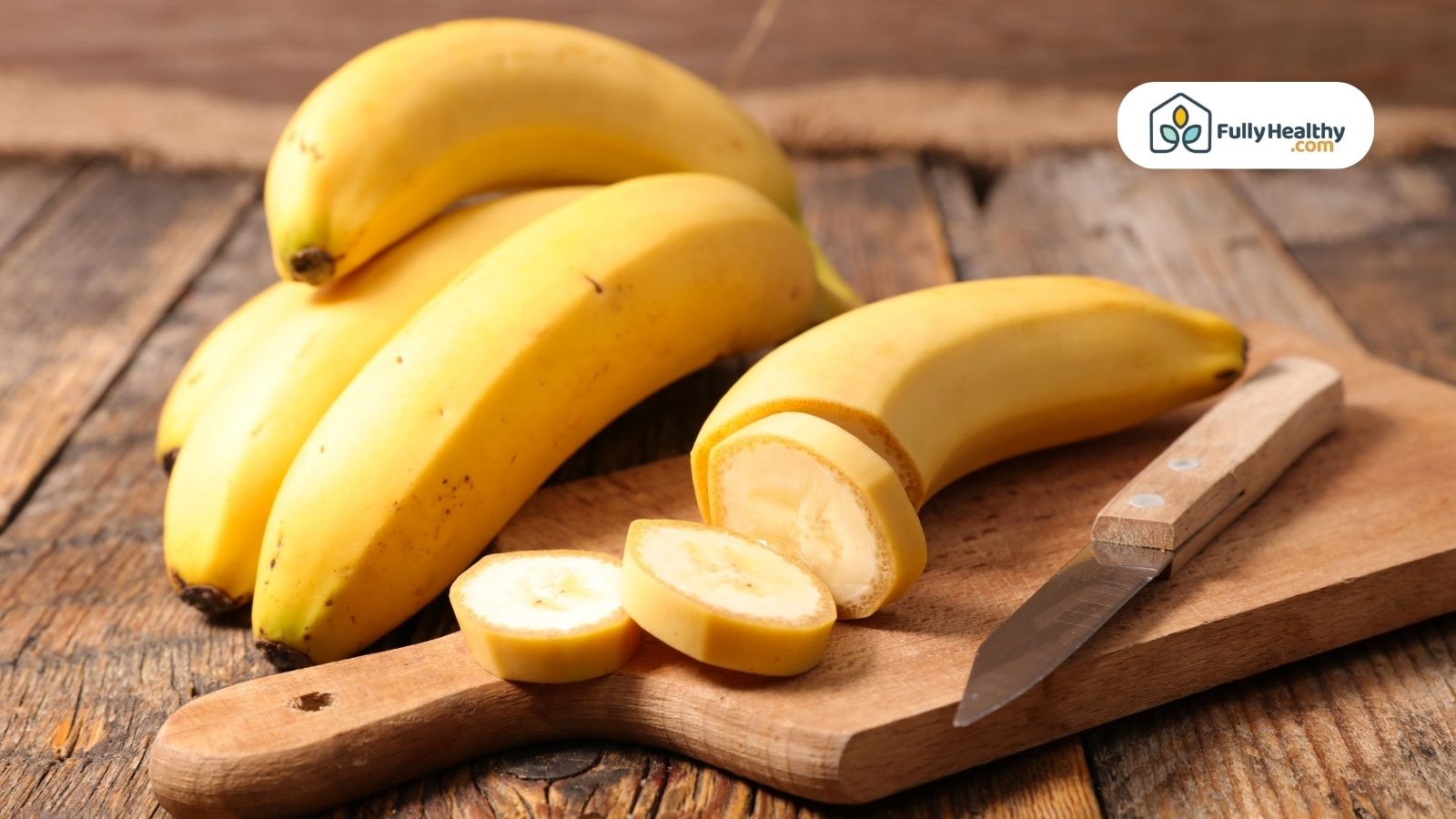 Sliced banana on wooden board with whole bananas and knife nearby