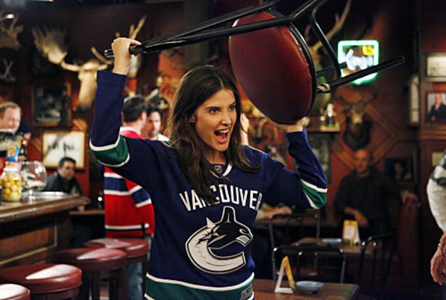 Robin en el bar canadiense, con la equipación de los Vancouver Canucks, rugiendo y levantando una silla por encima de la cabeza.