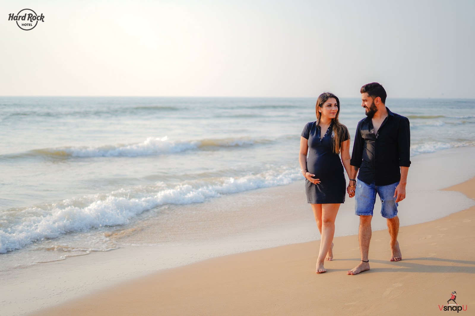 Expecting parents walking together on a beach at sunset, creating beautiful moments in a serene maternity shoot.