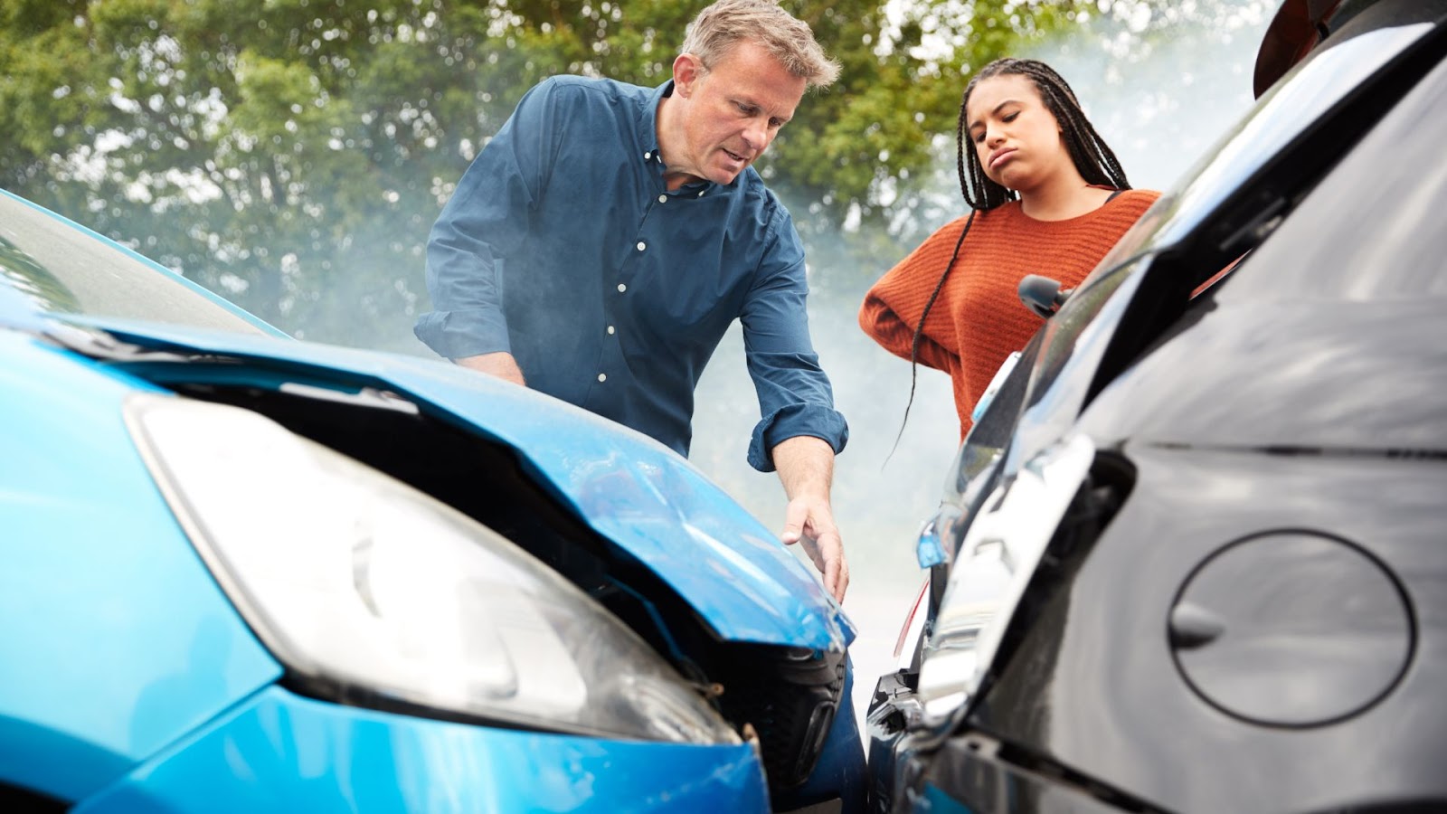 two people inspecting their cars after an accident