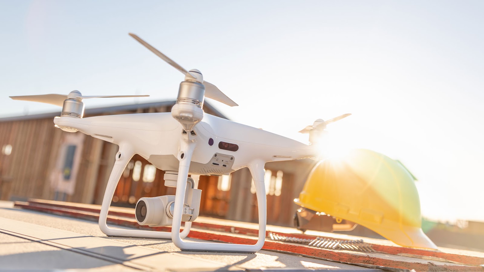 A white drone with a mounted camera on a construction site next to a yellow safety helmet, capturing aerial project data