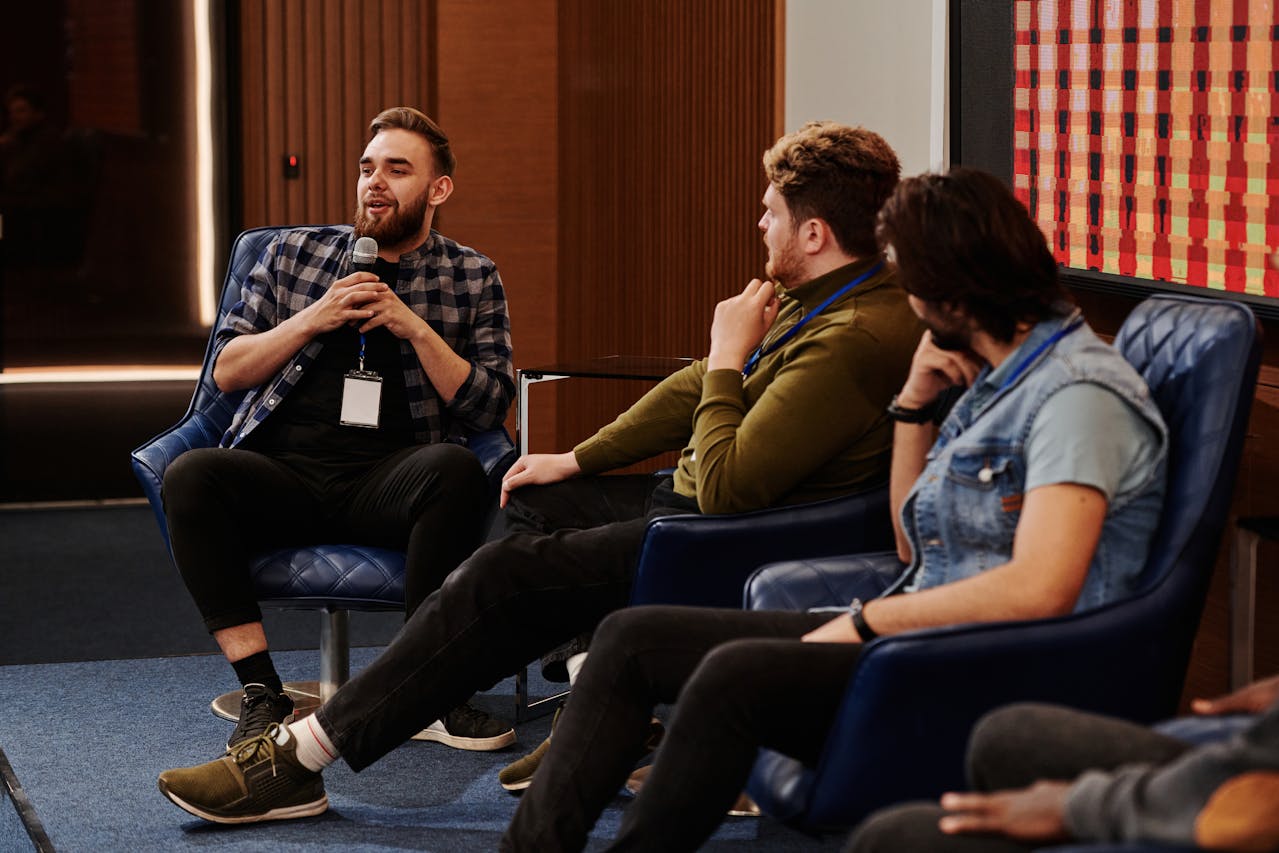 A group of people sitting in a panel discussing marketing automation best practices, with one person holding a microphone and speaking, while the others listen attentively in a casual environment