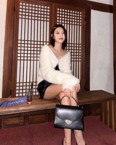 This contains a picture of Sooyoung sitting on top of a wooden bench holding a black purse next to a book