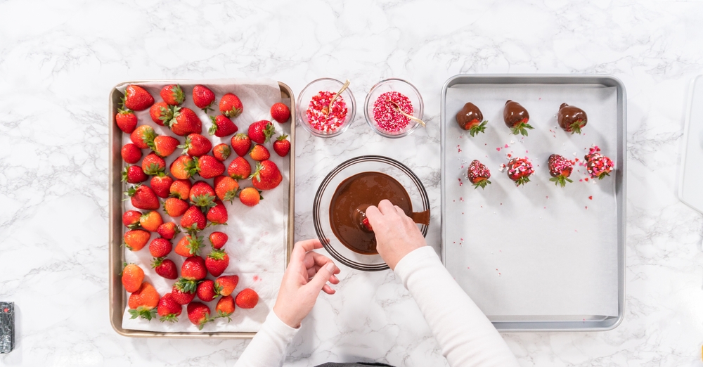 A woman following proper preparation techniques while making chocolate-covered strawberries