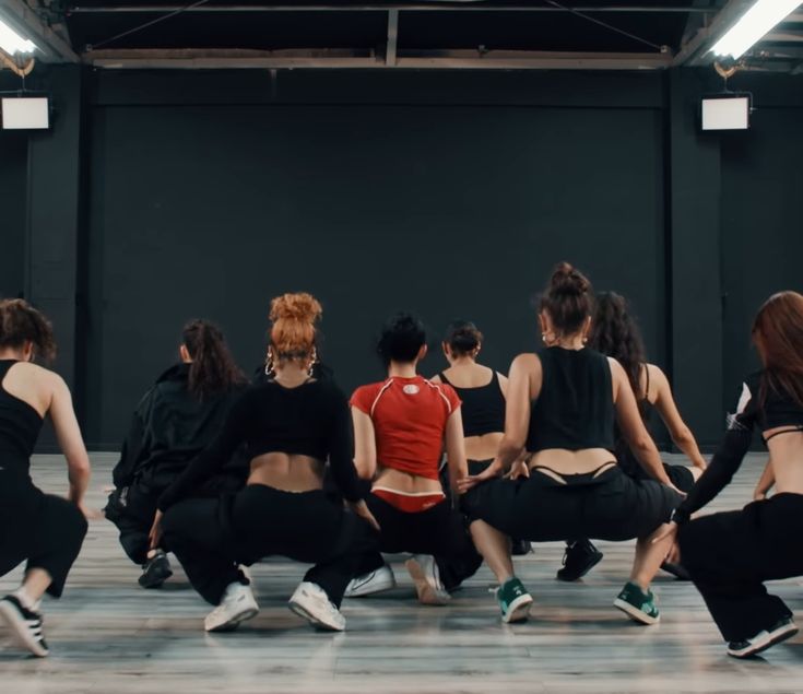 This contain: a picture of  BLACKPINK Jennie  in black and red shirts with other people they are doing squats on the floor