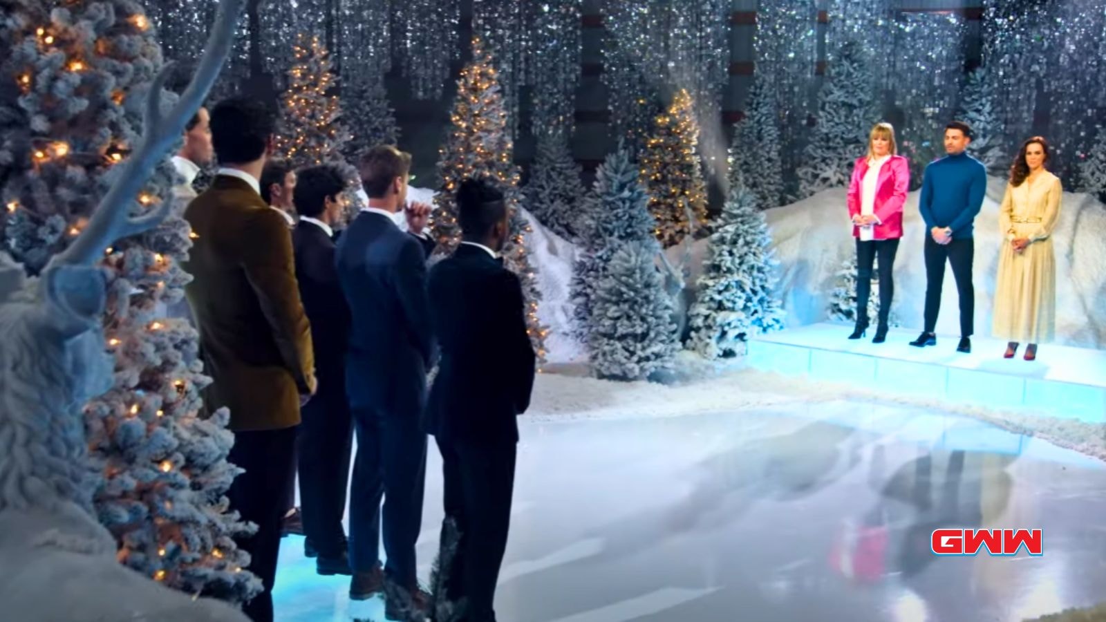 A snowy, festive stage scene with hosts addressing contestants in formal attire.