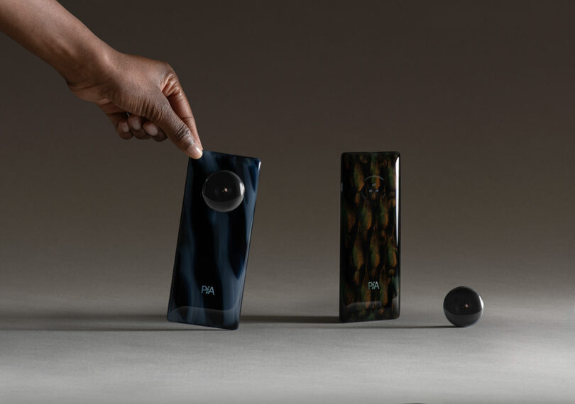 A hand holds a sleek, dark device labeled "PAA" next to another similar device and a detached circular LAYER component, all placed on a neutral surface.