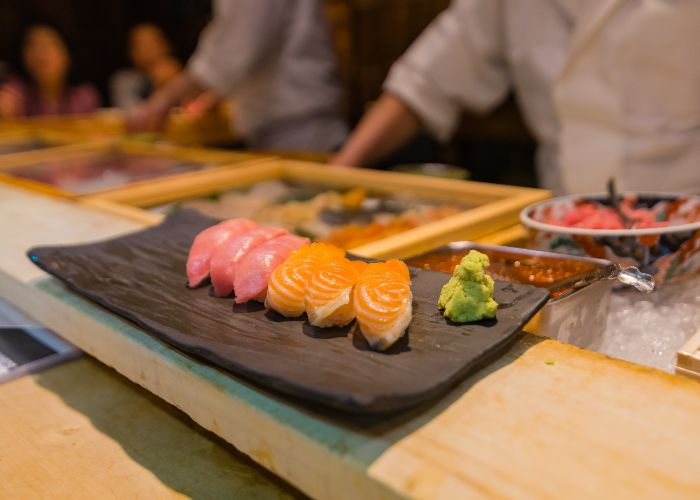 Five pieces of nigiri sushi on a slate serving tray, with a side of wasabi.