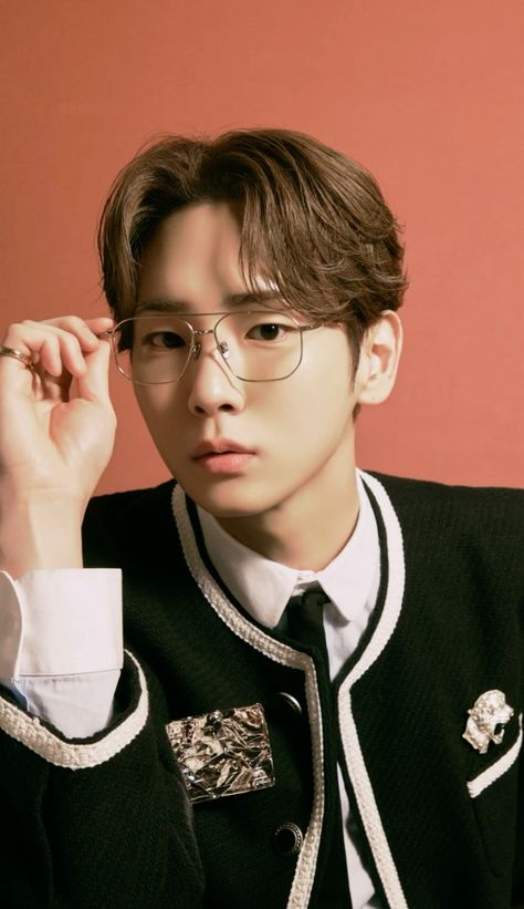 This  contain an image of  SHINee Key wearing glasses and a black sweater with white stripes on the collar, sitting in front of a red wall